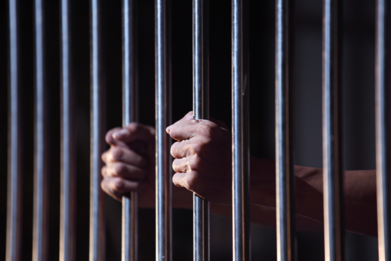 Hands holding bars of a prison cell.